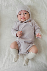 Baby wearing the Avauma Selina Babysuit in lavender haze, paired with a cozy hat and socks, emphasizing comfortable long-sleeves and breathable fabric perfect for infants.